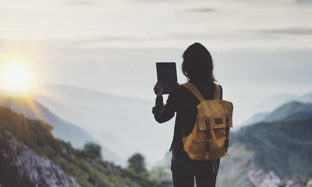 Hipster girl with backpack enjoying sunset on peak of foggy mountain, tourist traveler taking pictures of amazing landscape on mobile sell phone digital camera on background valley view mockupの写真素材