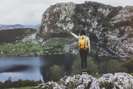 Hipster young girl with backpack enjoying sunset on peak of foggy mountain, looking on lake and poining hand. Tourist traveler on background valley landscape panoramic view mockup, sunlight in tripの写真素材