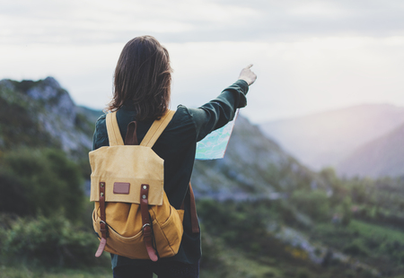 Hipster young girl with backpack enjoying sunset on peak of foggy mountain, looking a map and poining hand. Tourist traveler on background valley landscape panoramic view mockup, sunlight in tripの写真素材