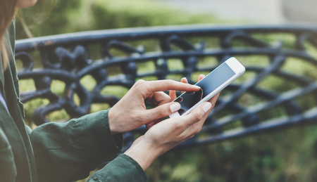 Hipster texting message on smartphone or technology, mock up of blank screen. Tourist girl using cellphone on forged steel bench background close. Female hands holding device. Mockup text messageの写真素材