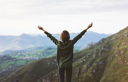 Happy tourist traveler standing on a rock with raised hands, hiker looking to a valley below in trip in spain, hipster young girl enjoying peak of foggy mountain background landscape view mockupの写真素材