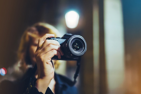 photographer girl enjoying night street in trip, traveler relax lifestyle concept, hipster hiker tourist making photo, holding in hands camera on background of evening atmospheric city, blogger view in holidayの写真素材