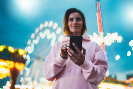 Person pointing finger on screen smartphone on defocus background bokeh light in evening street, hipster girl using in hands mobile phone gadget in night atmospheric city illumination, online wifi internet conceptの写真素材