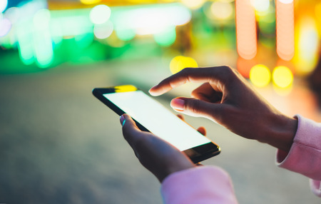 Girl pointing finger on screen smartphone on background bokeh light in night atmospheric city illumination in evening street defocus, hipster using in hands mobile phone, lifestyle online wifi internet conceptの写真素材