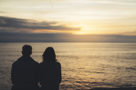 Couple hugging on background beach ocean sunrise, meeting of lovers concept, silhouette two romantic people cuddling and looking on view evening seascape, hipster enjoy sunset together, travel holidays vacation relaxの写真素材