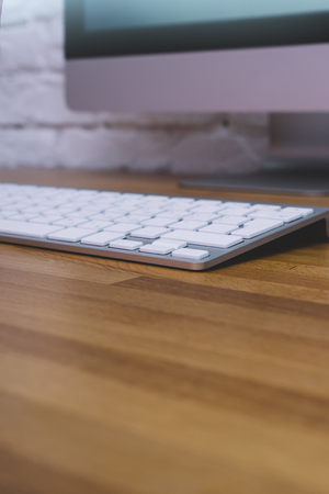 Side view of a computer monitor with a blank screen on a pure white background of a brick wall and a keyboard on a wooden table with, blank for your text or content or design, closeup, free spaceの写真素材