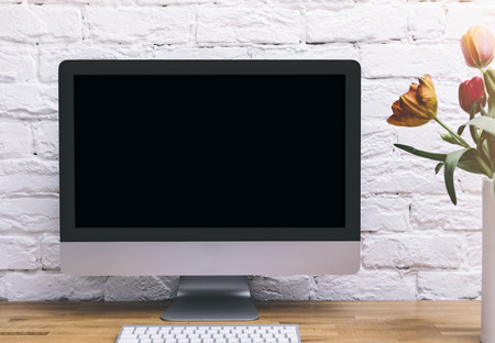 Computer monitor with blank screen on a pure white background of a brick wall and a keyboard on a...