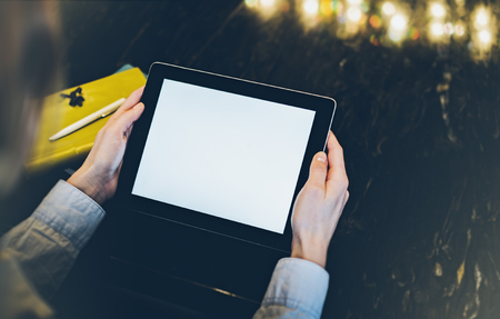 Closeup of a woman pointing finger to an blank display of the tablet with a blue color in a homelike atmosphere on warm bokeh background lighting color, female hends using computer in cafe with reflection and glareの写真素材