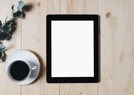 Tablet with a clean blank screen monitor with a branch of eucalyptus and a cup of coffee on a wooden background with natural wood planks top view horizontal, digital computer with blank template copy space screen for your information or content, touch pad with empty display and space for publicity information or advertising textの写真素材