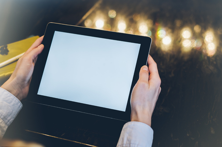 Closeup of a woman pointing finger to an blank display of the tablet with a blue color in a homelike atmosphere on warm bokeh background lighting color, female hends using computer in cafe with reflection and glareの写真素材