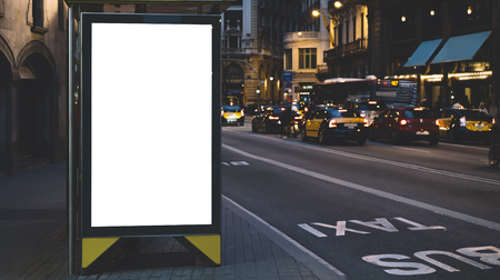 Blank advertising light box on bus stop, mockup of empty ad billboard on night bus station, template banner on background city street for poster or sign in Barcelona, afisha board and headlights of taxi carsの写真素材