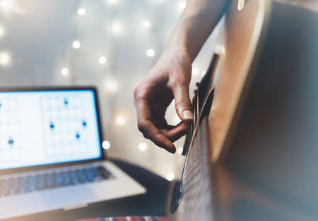 Hipster playing guitar in home atmosphere, person studying on musical instrument, notes in laptop on background glow bokeh Christmas illimination, female hands in holiday on relax glitter decoration, blurの写真素材