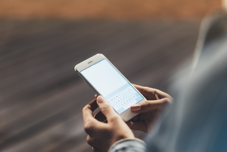 Girl pointing finger on screen smartphone on background wooden floor in night atmospheric city, hipster using in female hands and texting mobile phone, mockup glitter street lifestyle, blured backdropの写真素材