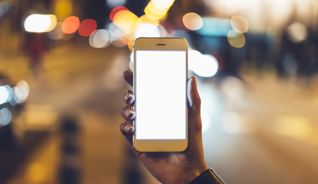 hipster hold in hands clean gadget mobile phone closeup, blank screen smartphone on background bokeh light in night atmospheric city, mockup street, lifestyle online wifi internet concept, lights auto taxiの写真素材