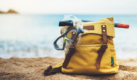 Hipster hiker tourist yellow backpack and swimming mask on background blue sea ocean horizon on sand beach, blurred panoramic seascape blank, traveler relax holiday concept, sunlight view in trip vacationの写真素材