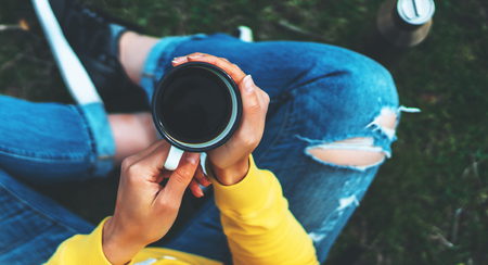 Top view girl holding in hands cup of hot tea on green grass in outdoors nature park, beautiful woman hipster enjoy drinking cup of coffee, lifestyle relax recreation meditation conceptの写真素材