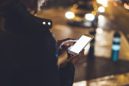Girl pointing finger on screen smartphone on background bokeh light in night atmospheric city street, blogger hipster girl using in hands mobile phone, lights auto taxi; lifestyle online wifi internet conceptの写真素材
