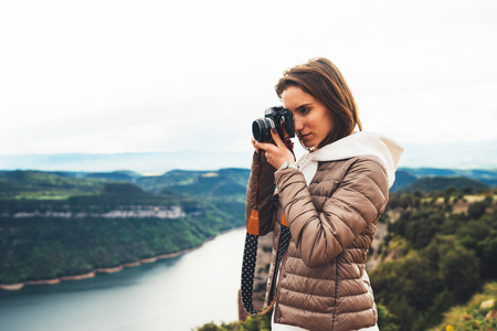 photographer traveler on green top on mountain, tourist looking holding in hands digital photo camera, hiker taking click photography, girl enjoy nature panoramic landscape in trip, relax holiday hobby conceptの写真素材