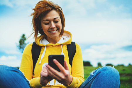 tourist young smile girl on background green grass using mobile smartphone, women holding in female hands gadget technology, hiker texting finger message on screen content online wifi internet lifestyle conceptの写真素材