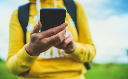 tourist girl on background green grass using mobile smartphone closeup, women holding in female hands gadget technology, hiker texting finger message on screen content online wifi internet lifestyle conceptの写真素材