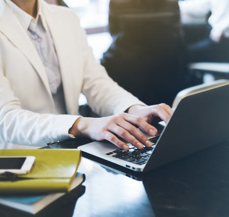 Young woman writing text hands on the open laptop in a cafe on a table with reflection and glare , businesswoman working on computer and smartphone in blue tonesの写真素材