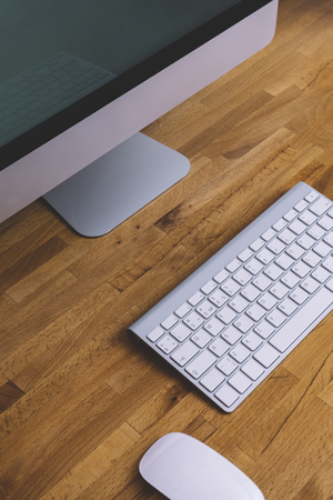 Top view of a computer monitor with a blank screen on a pure white background of a brick wall and a keyboard and mouse on a wooden table, blank for your text or content or design, closeup, free spaceの写真素材