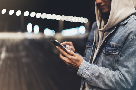 Girl pointing finger on screen smartphone on background illumination bokeh color light in night...