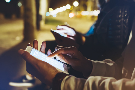 People together pointing finger on screen smartphone on background bokeh light in night atmospheric city, group adult hipsters friends using in hands modern mobile phone closeup, street online wi-fi internet conceptの写真素材