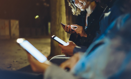 People together pointing finger on screen smartphone on background bokeh light in night atmospheric city, group adult hipsters friends using in hands modern mobile phone closeupの写真素材