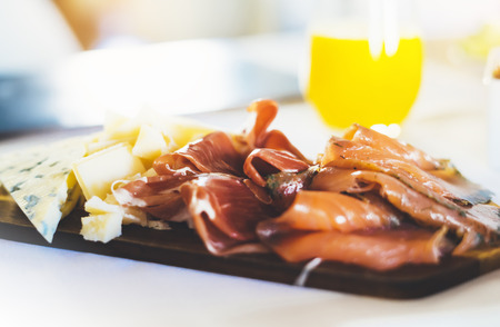 Prosciutto, parmesan on wooden board on kitchen table, blur concept, spanish breakfast with serrano jamon and gorgonzola cheese closeup, traditional food on restaurant or cafeの写真素材
