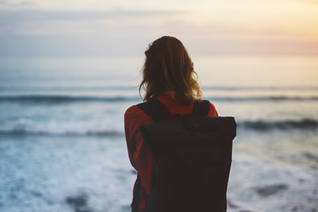 Hipster hiker tourist with backpack looking of amazing seascape sunset on background blue sea, photographer enjoying ocean horizon, blurred panoramic sunrise blank mockup, traveler relax holiday concept, sunlight view in trip vacation northern spainの写真素材