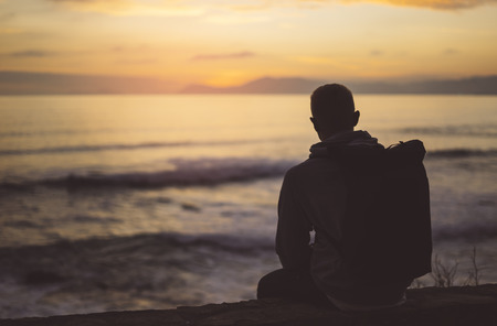 Hipster hiker tourist with backpack looking of amazing seascape sunset on background blue sea, guy enjoying ocean horizon, blurred panoramic sunrise blank mockup, traveler relax holiday concept, sunlight view in trip vacation northern spainの写真素材