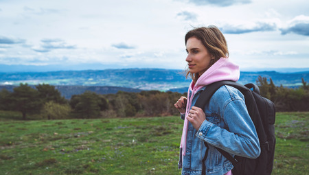 tourist traveler with black backpack standing on green top on mountain, hiker looking on hills and mountain, girl enjoying nature panoramic landscape in trip, relax holiday concept in trekking tripの写真素材