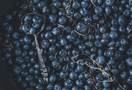 Blueberries on vintage wooden black background top view, healthy food on dark table mockup, berry for smoothie with vintage metal spoon isolated on rustic country board, fresh nutrition mock up closeup, copy space for text designの写真素材
