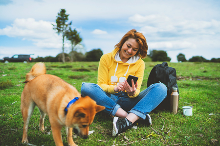 tourist smile girl on background nature landscape using mobile smartphone with friends dog, person holding in hands gadget technology, text message on screen online wifi internet lifestyle conceptの写真素材