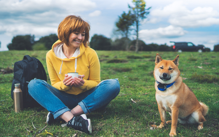 Happy smile girl holding in hands cup drink, red japanese dog shiba inu on green grass in outdoors nature park, beautiful young woman hipster and dogs friends, friendship lifestyle relax recreation meditation conceptの写真素材
