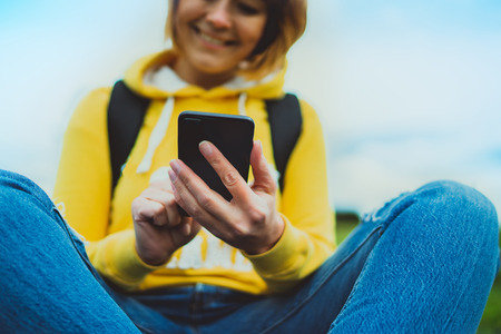 tourist young smile girl on background green grass using mobile smartphone, women holding in female hands gadget technology, hiker texting finger message on screen content online wifi internet lifestyle conceptの写真素材