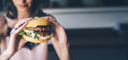 Young girl holding in female hands fast food burger, american unhealthy calories meal on background, mockup with copy space for text message or design, hungry human with grilled hamburger front viewの写真素材