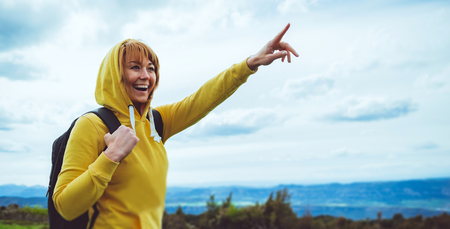 tourist traveler with backpack on background mountain blue sky clouds, hiker looking in distance, girl enjoying nature panoramic landscape and pointing hands, relax holiday mockup concept in trekking tripの写真素材