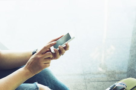 Young hipster girl at airport and put feet in yellow boot on suitcase waiting air flight, female hands holding touch smart phone in terminal departure lounge gate, traveler trip concept, mockup of blank screen sellphoneの写真素材