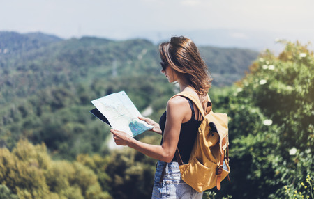 Hipster young girl with bright backpack enjoying panoramic mountain sea, using map and looking distance. Tourist traveler on background landscape Barcelona view mockup, sun flare in trip holidayの写真素材