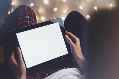 Hipster girl using tablet technology in home atmosphere, person holding computer on background glow bokeh Christmas illimination, female hands texting on relax glitter xmas decoration, mockup templates, blurの写真素材