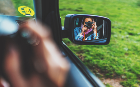 tourist girl in an open window of a car taking photography click on retro vintage photo camera, photographer looking on reflection in a mirror auto, blogger using hobby content concept, enjoy tripの写真素材