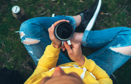 Top view girl holding in hands cup of hot tea on green grass in outdoors nature park, beautiful woman hipster enjoy drinking cup of coffee, lifestyle relax recreation meditation conceptの写真素材
