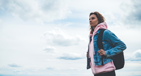 tourist traveler with black backpack on background mountain, hiker looks up at blue sky clouds, girl enjoying nature panoramic landscape in trip, relax holiday mockup concept in trekking tripの写真素材
