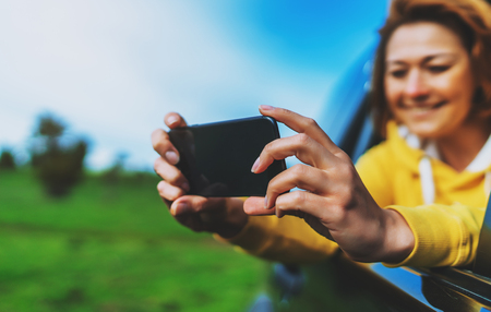 smile tourist girl in an open window of a auto car taking photo selfie on mobile smart phone, person looking on camera gadget technology, blogger using content online wifi internet conceptの写真素材