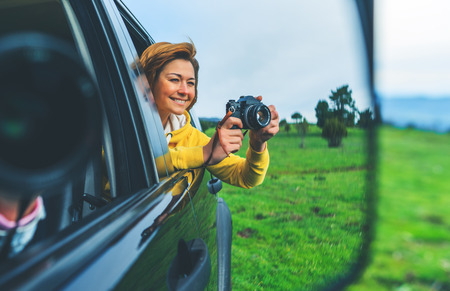 smile tourist girl in an open window of a auto car taking photography click on retro vintage photo camera, photographer looking on camera technology, blogger using hobby content concept, enjoy tripの写真素材