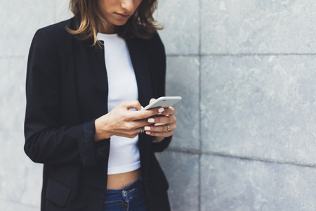 Portrait young businesswomen in black suit using smartphone isolated on background concrete gray wall mockup, pretty hipster manager holding mobile gadget, girl smiletexting message, connectの写真素材