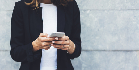 Portrait young businesswomen in black suit using smartphone isolated on background concrete gray wall mockup, pretty hipster manager holding mobile gadget, girl smiletexting message, connectの写真素材