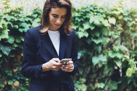 Portrait young businesswomen in black suit using smartphone isolated on background green nature wall mockup, pretty hipster manager holding mobile gadget, girl smile and texting message, connectの写真素材